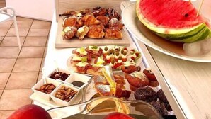 A buffet table with various food items including pastries, fruits, and a watermelon slice. - Don Carlo Tropea (Tropea)