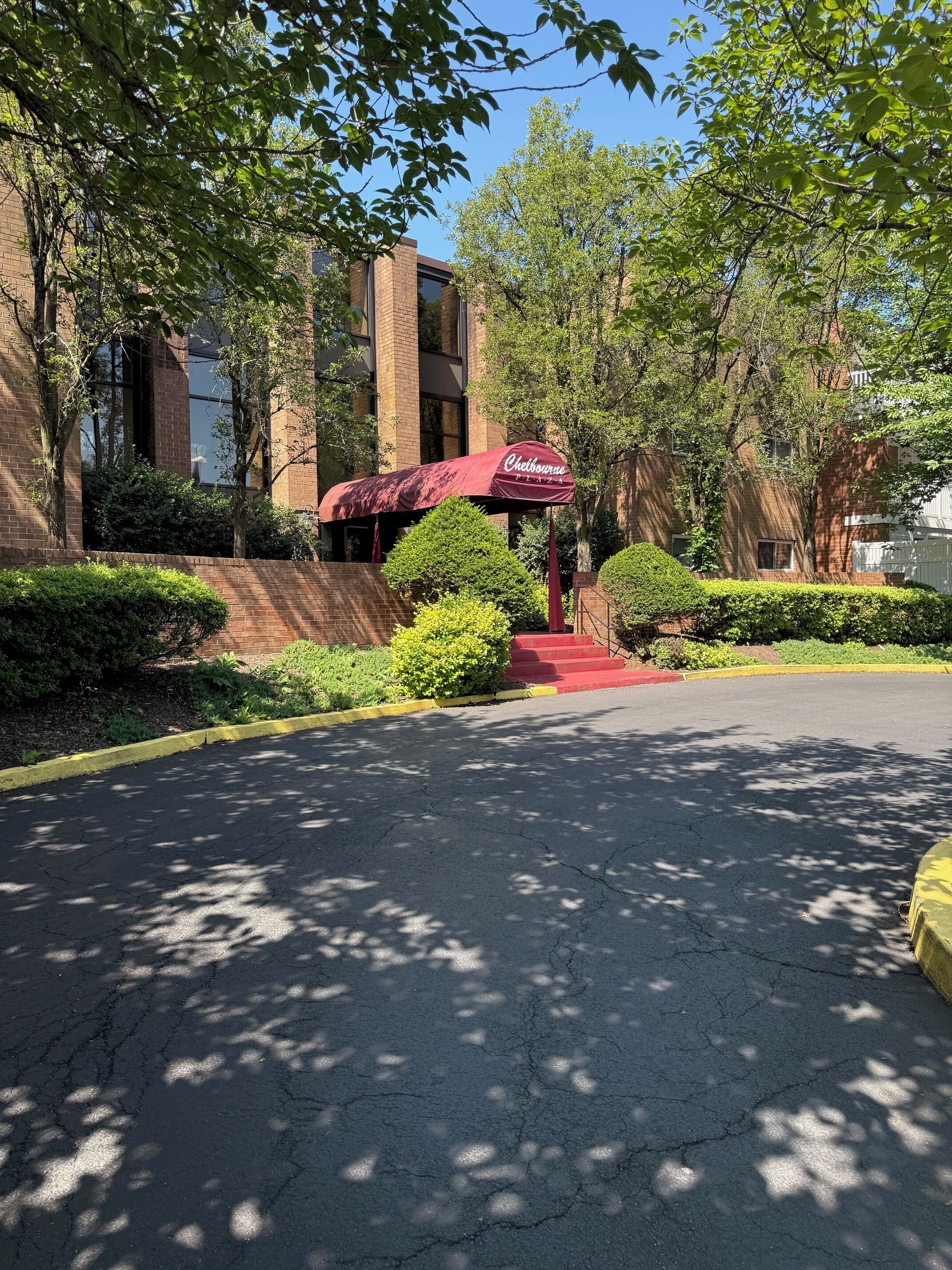 A parking area with a red umbrella, a brick building, and greenery.