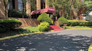 A parking area with a red umbrella, a brick building, and greenery.