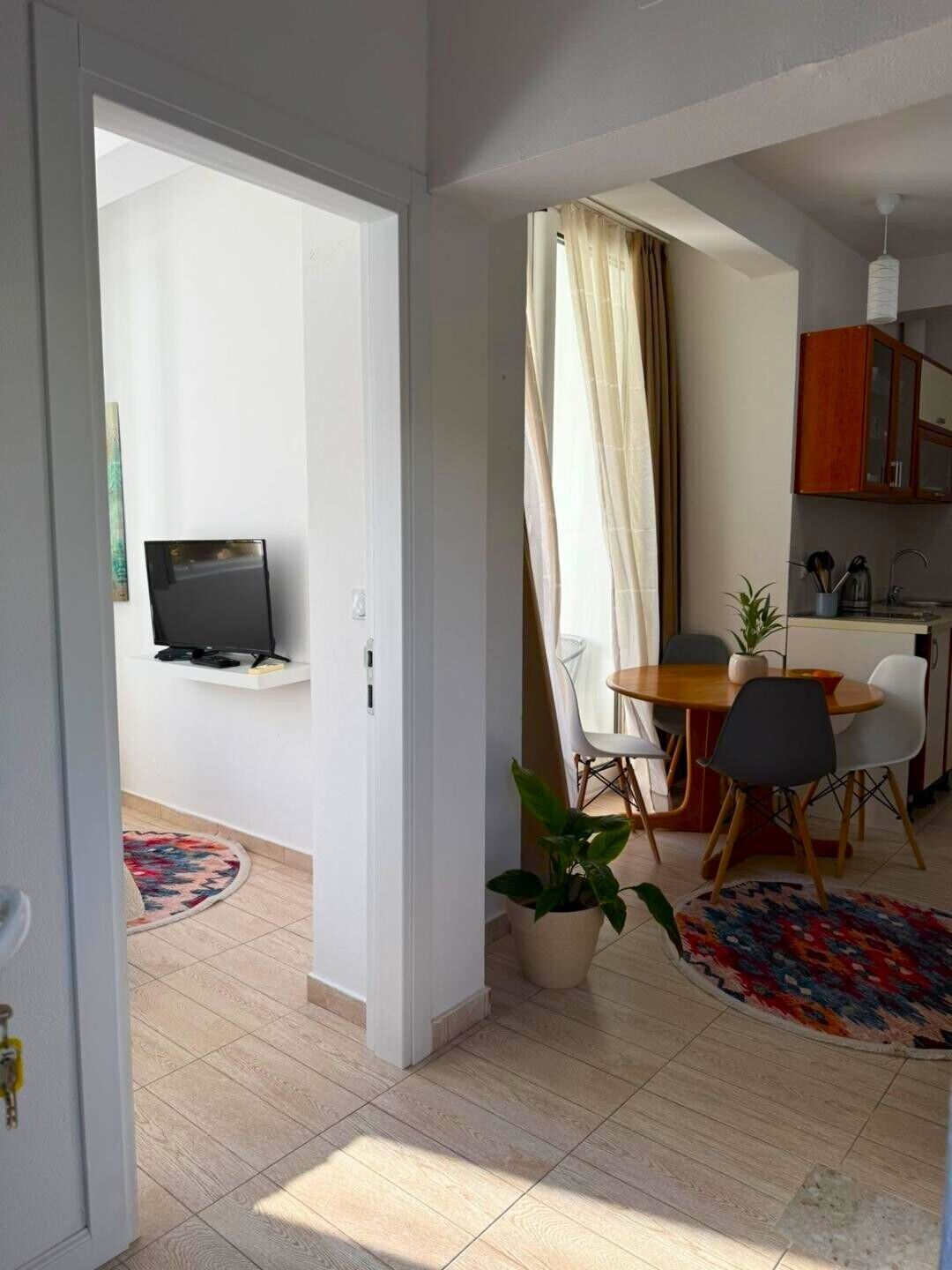 A modern living space with a dining area, a television mounted on a wall, and a kitchen area with cabinets.
