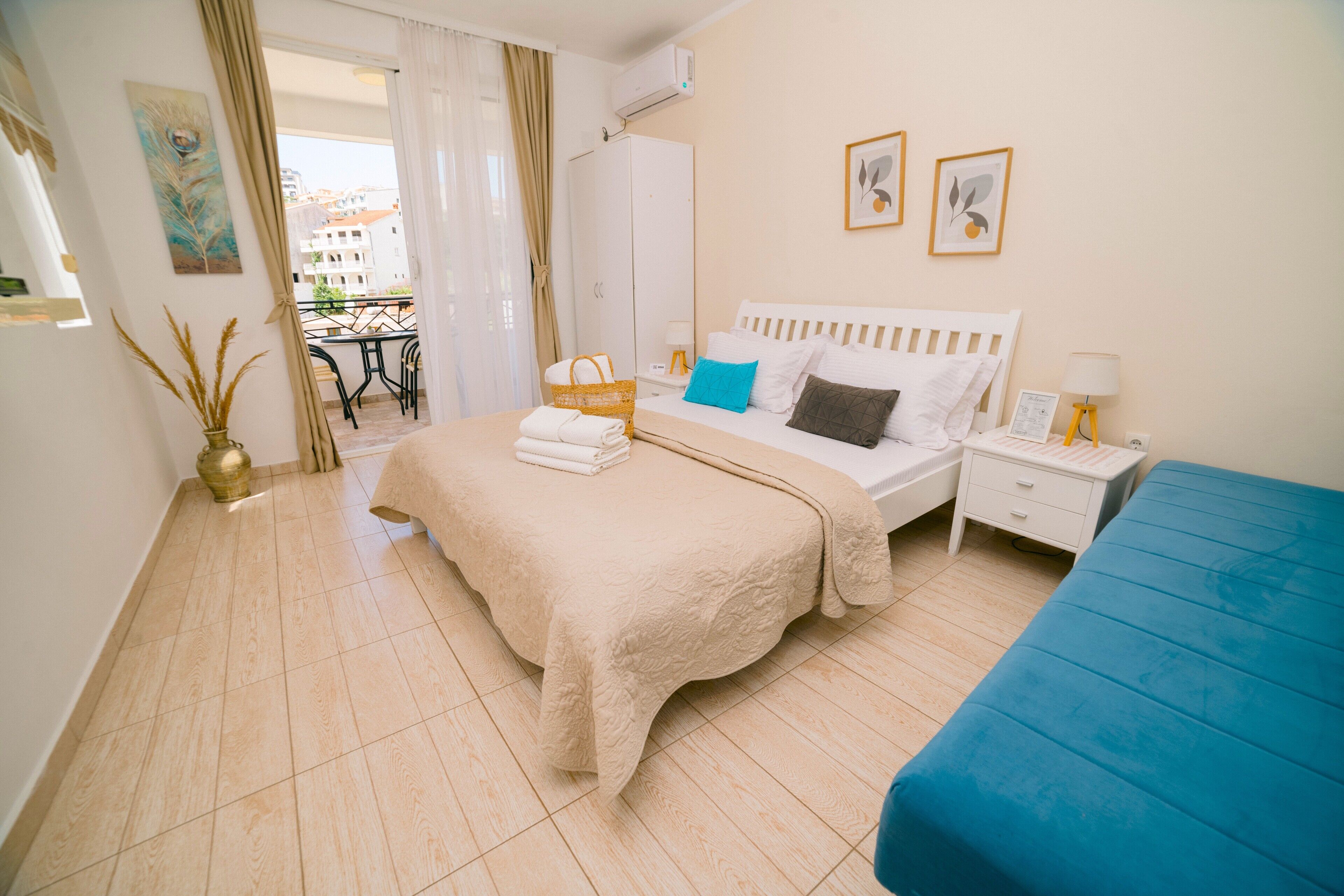 Una habitación de hotel con cama, mesita de noche, ventana con cortinas, vista al balcón y un cuadro en la pared.