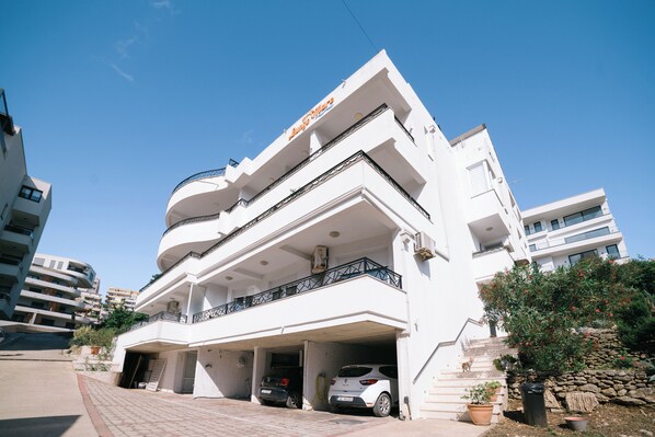 A modern multi-story building with a white facade, balconies, and a parking garage. - Deluxe Studio Apartment with Sea view (Ulcinj)