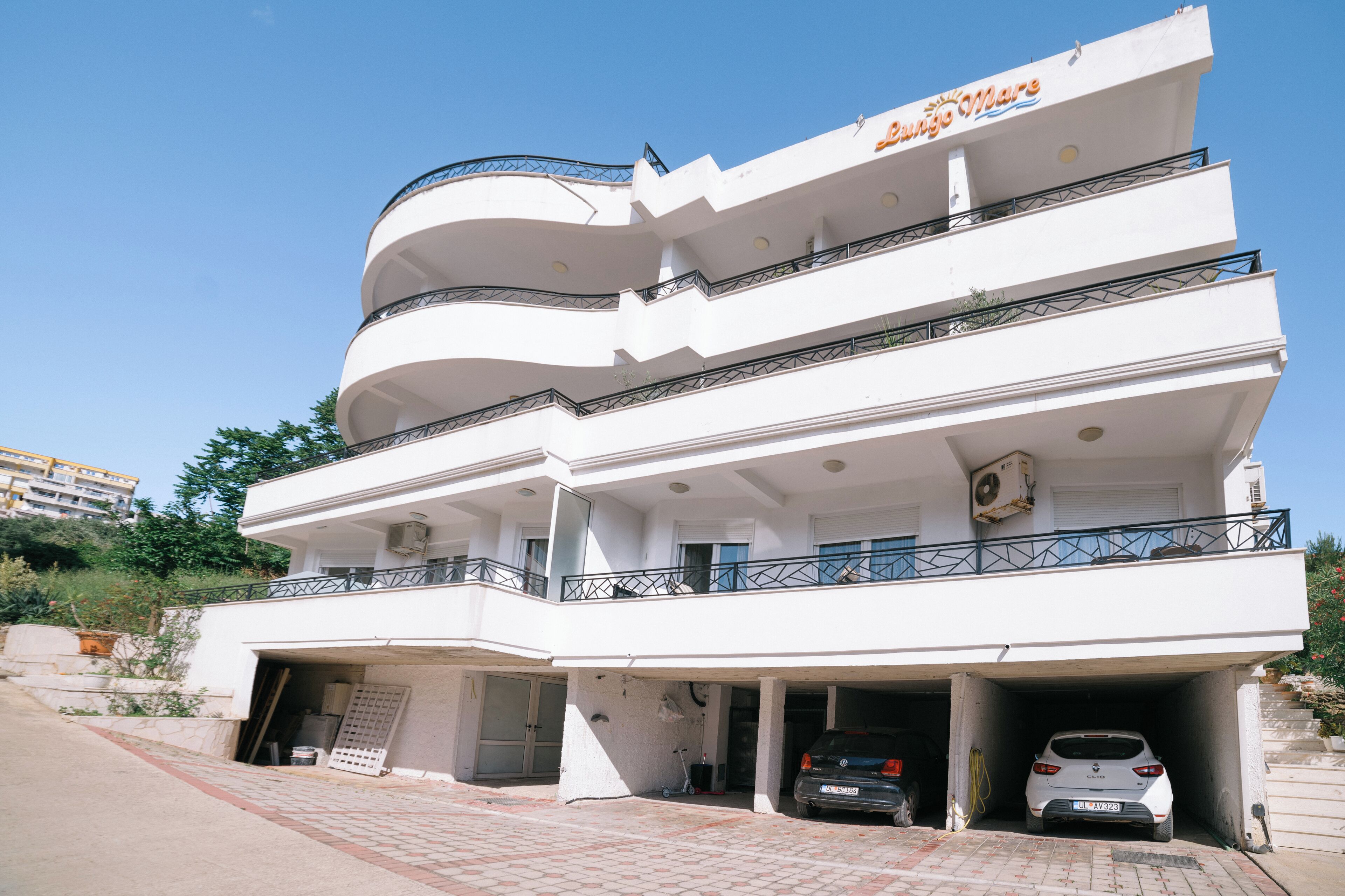 A multi-story building with a white facade, balconies, and two parking garages.