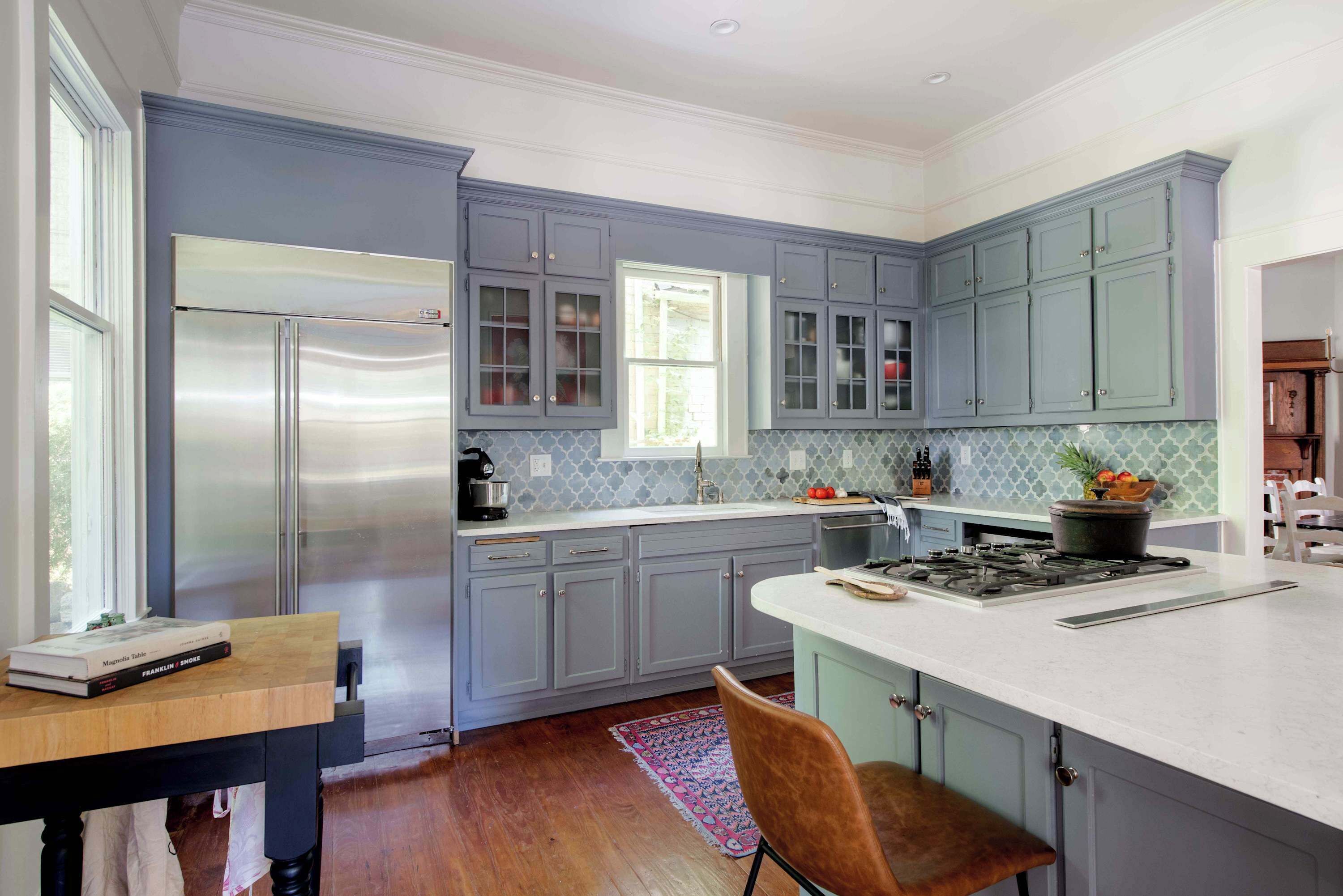 A modern kitchen with grey cabinets, a stainless steel refrigerator, and a central island with a stove.
