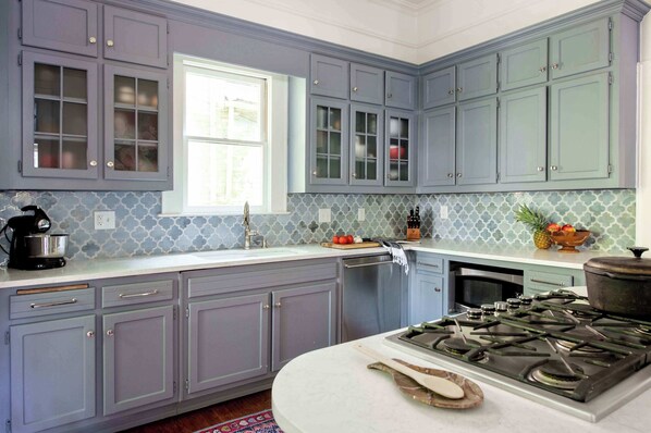 Una cucina con pensili azzurri, un piano cottura in acciaio inossidabile e una finestra che lascia entrare luce naturale.