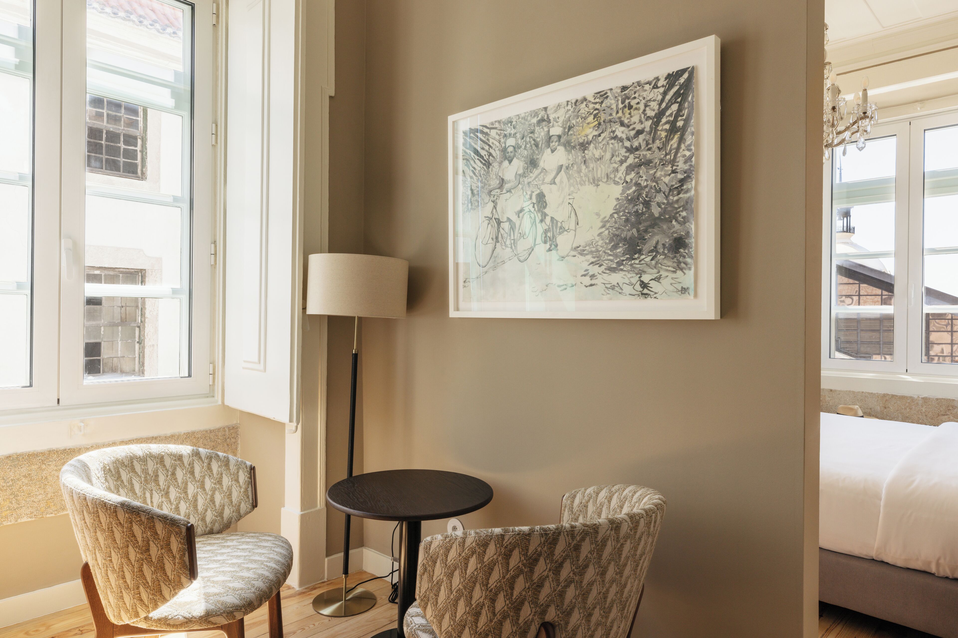 Habitación de hotel con dos sillones estampados, una mesita redonda pequeña, una lámpara de pie y una obra de arte grande en la pared.