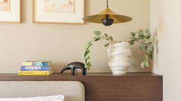 Een keurig opgemaakt hotelkamer met een bed, een nachtkastje met een lamp, ingekaderde foto's aan de muur en een klein plankje met boeken en decoratieve objecten.