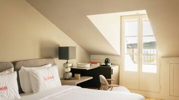 A hotel room with a bed, a desk, a chair, a lamp, and a window with a view of a balcony.