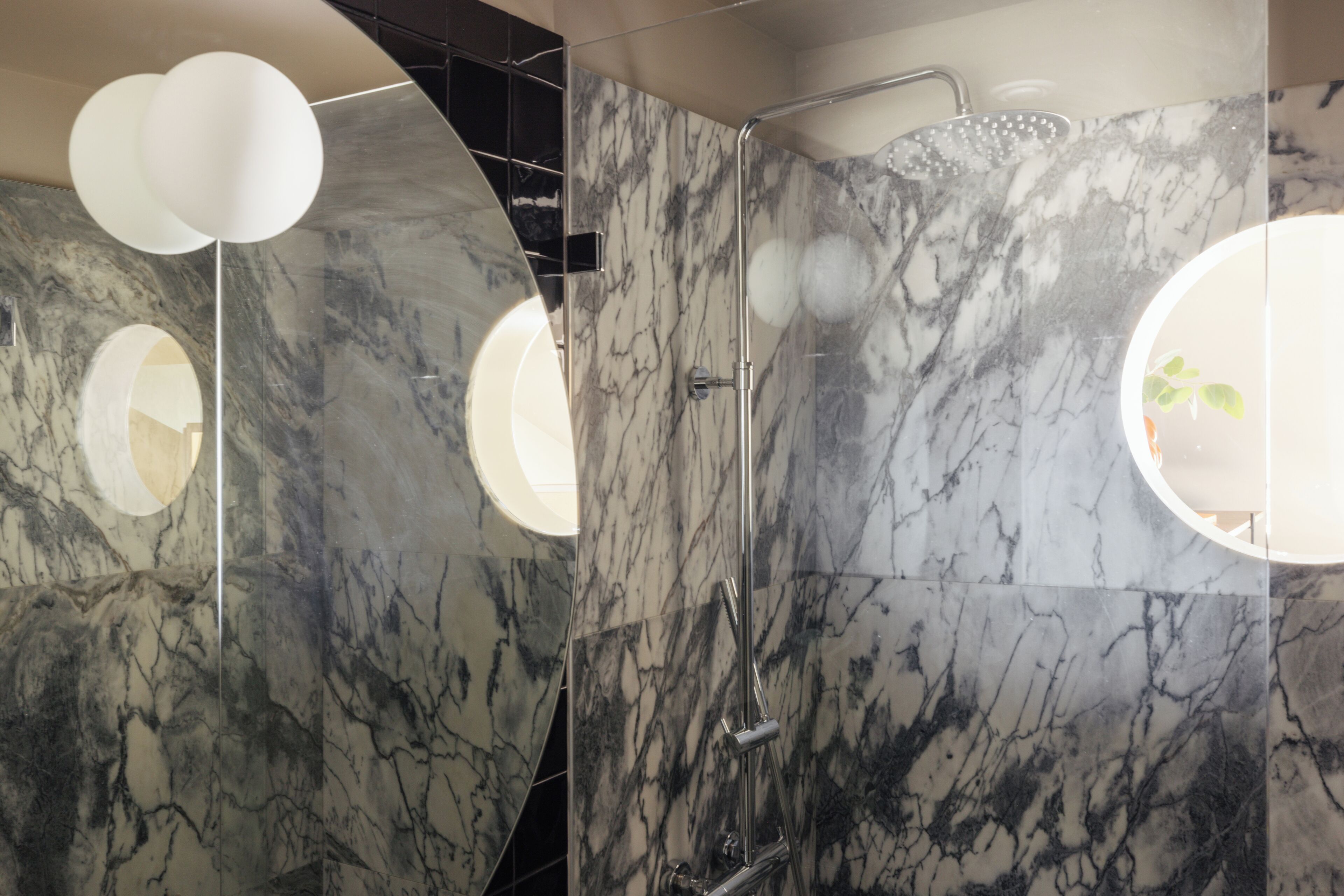 A modern bathroom with marble walls, a shower, and two circular light fixtures.
