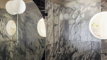 A modern bathroom with marble walls, a shower, and two circular light fixtures.