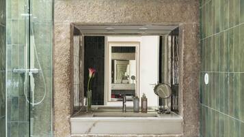 Un baño con ducha de vidrio, lavamanos de mármol y paredes con azulejos verdes.