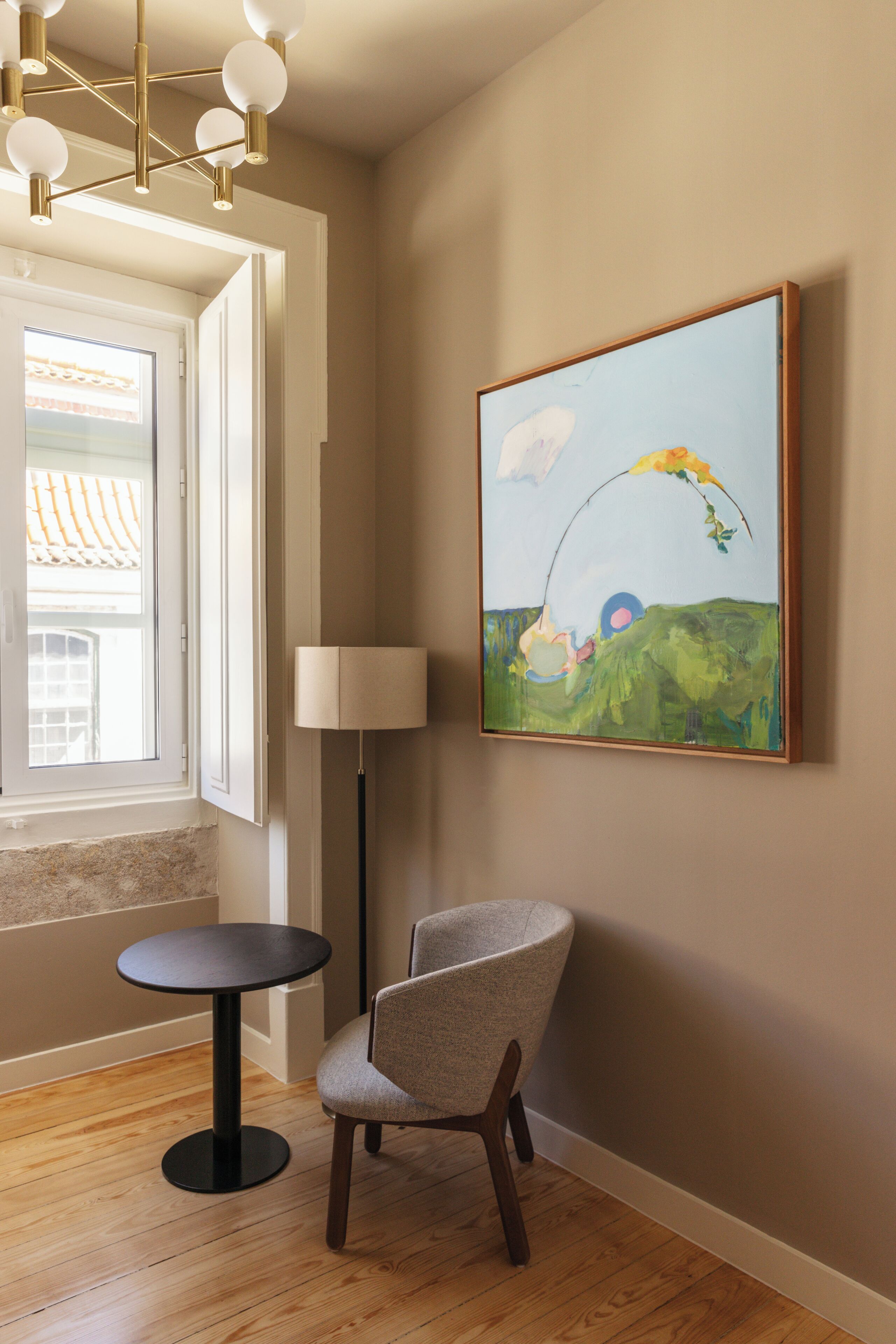 A room with a round table, a chair, a floor lamp, and a painting on the wall.