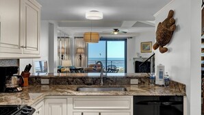 A kitchen with a granite countertop, white cabinetry, a built-in stove, and a view of the ocean through a large window. - Award-Winning Resort Amenities | Shipwatch 408A (Isle of Palms)