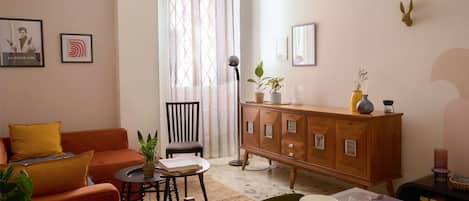 A living room with a sofa, a dining table set with plates and glasses, a wooden cabinet, and a chair.