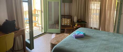 Habitación de hotel con cama, escritorio, silla, una mesita con fruta y vistas a través de una puerta corredera.