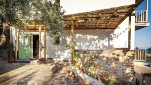 A stone-paved courtyard with a wooden pergola, a green door, and a stone wall with plants. - Pelikastri (South Pelion)