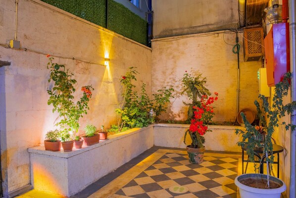 Piso xadrez com plantas em vasos e luminária fixada na parede.