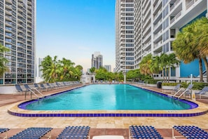 Una piscina con sillas de descanso, rodeada de edificios altos y palmeras.