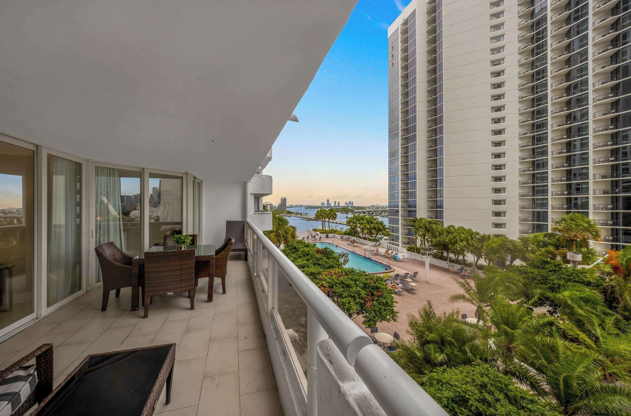 A balcony with a dining area, a pool, and a view of a city skyline.