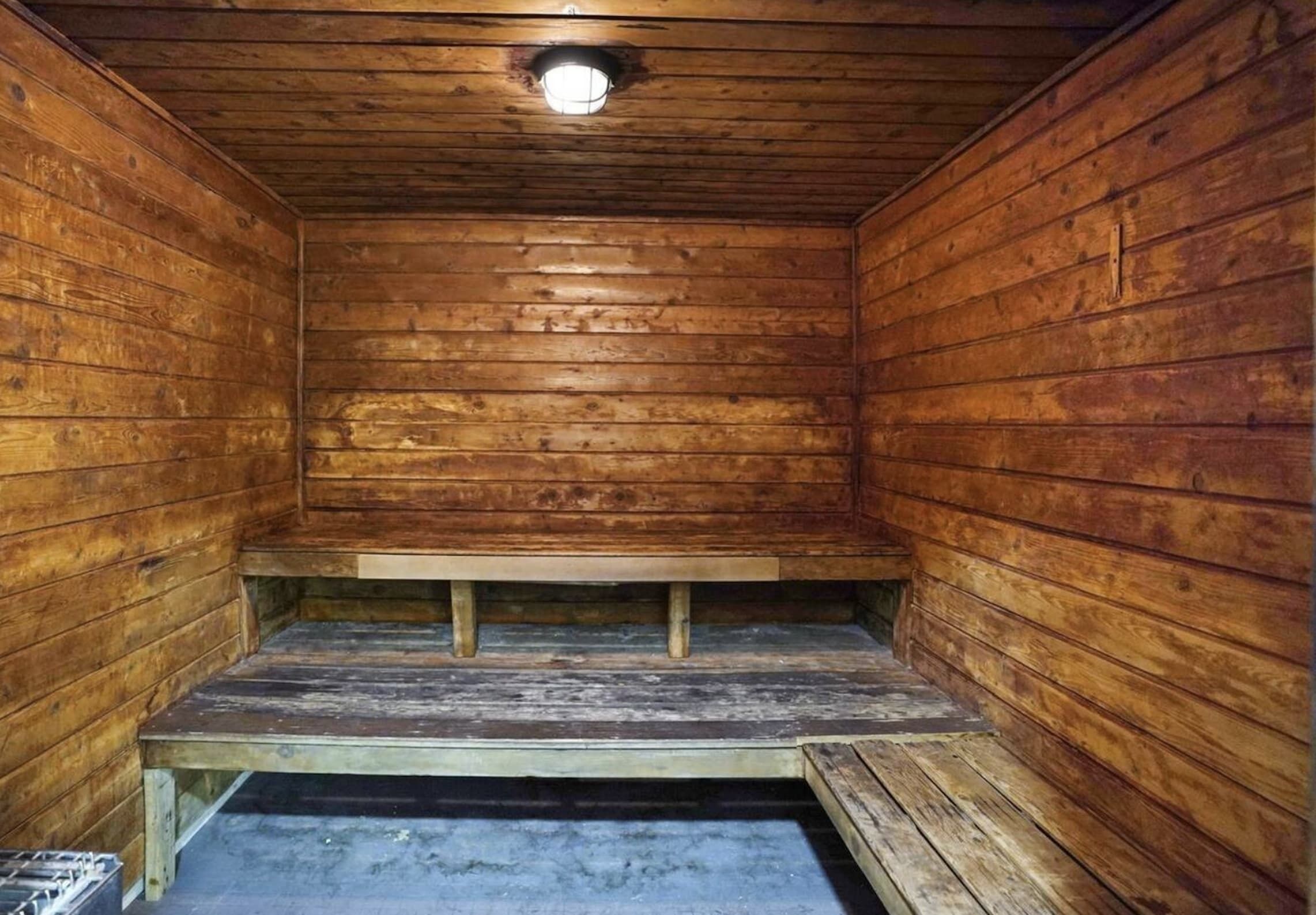 A wooden cabin interior with a bench at the center, a small window at the top, and a concrete floor.