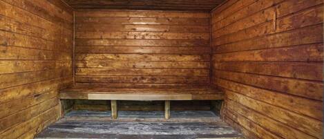 A wooden cabin interior with a bench at the center, a small window at the top, and a concrete floor.