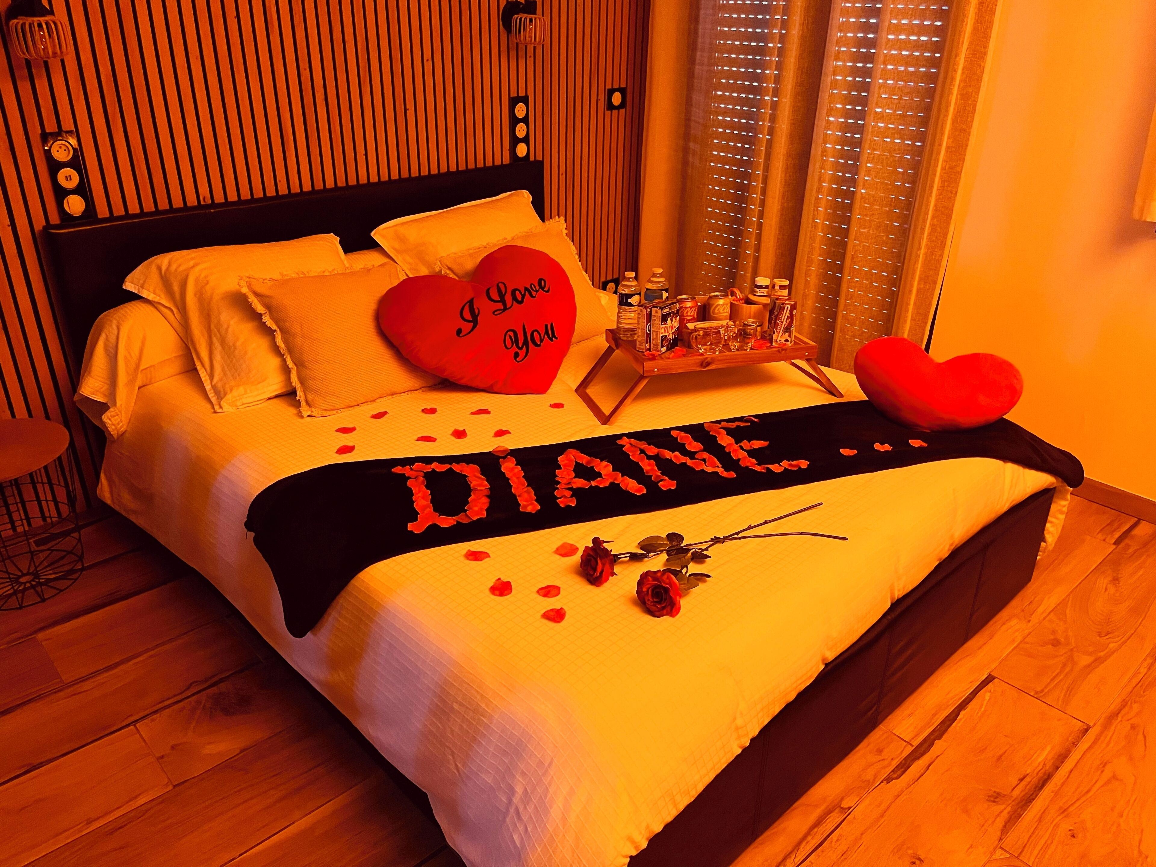 En säng med en hjärtformad kudde, ett bricka med diverse föremål och en filt med namnet ”DIANE” på.