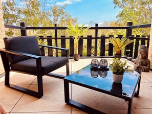 Un balcon avec une chaise, une table, des plantes en pot et une statue de Bouddha.