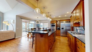 A spacious kitchen with wooden cabinets, a central island, stainless steel appliances, and pendant lighting. - Luxurious, Village Center Home! (Sun Peaks)