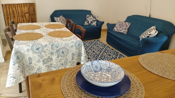 A dining area with a table set for four, a blue sofa, and a patterned rug. - Rosa's House Historic Center (Orosei)