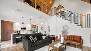 A spacious living area with a dark sofa, a coffee table, and a staircase leading to an upper level. - Entertainment Cabin Retreat, Spa Games & Play Zone (Broken Bow)
