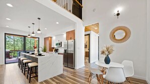 A modern kitchen with a central island, wooden flooring, and a dining area with white chairs. - Entertainment Cabin Retreat, Spa Games & Play Zone (Broken Bow)