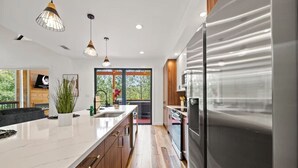 A modern kitchen with a large island, stainless steel appliances, pendant lighting, and a view to the outdoors. - Entertainment Cabin Retreat, Spa Games & Play Zone (Broken Bow)