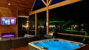 A wooden deck with a hot tub, a TV screen, and a view of the night sky. - Entertainment Cabin Retreat, Spa Games & Play Zone (Broken Bow)