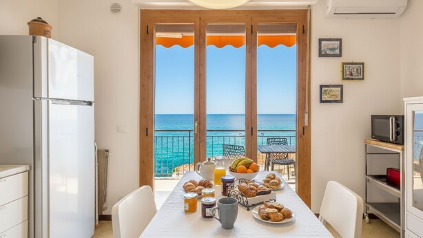 Una cocina con vista al mar, una mesa lista para el desayuno y un refrigerador.