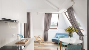 A modern kitchen with a built-in stove, a dining area with a round table and chairs, and a living space with a sofa and a view of the city. - Mariinsky Boutique Hotel (Batumi)