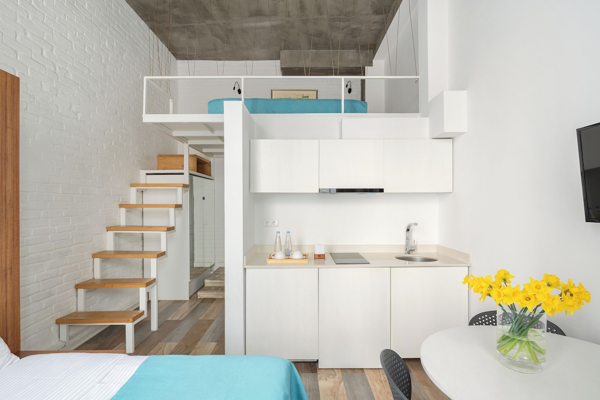 A compact, modern apartment with a loft bedroom, a kitchenette, and a dining area.