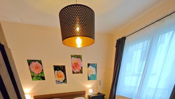 Ein Schlafzimmer mit einem großen Bett, einer Hängeleuchte, einem Nachttisch mit Lampe und einem fenster mit Vorhängen.
