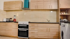 Una cocina moderna con armarios de madera, horno integrado, lavadora y una encimera con batidora y hervidor.