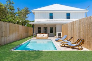 A white house with a swimming pool, a wooden fence, and a lawn.