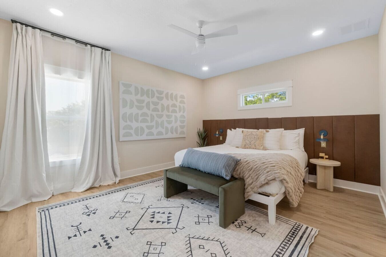 Une chambre à coucher comprenant un lit, des tables de chevet, un ventilateur de plafond et une grande fenêtre avec des rideaux.