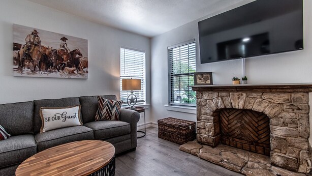 A living room with a stone fireplace, a gray sofa, a wooden coffee table, and a mounted TV. - Blue Wave Cottage Sum (Corpus Christi)