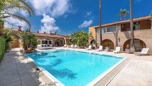A swimming pool surrounded by lounge chairs and palm trees, with a building featuring arched windows and a tiled roof in the background. - 3997 Villa Thalissa by Barbarhouse (Taranto)