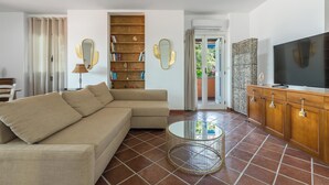 A living room with a beige sectional sofa, a round coffee table, a bookshelf, a television, and a sliding glass door leading to a balcony. - 3997 Villa Thalissa by Barbarhouse (Taranto)
