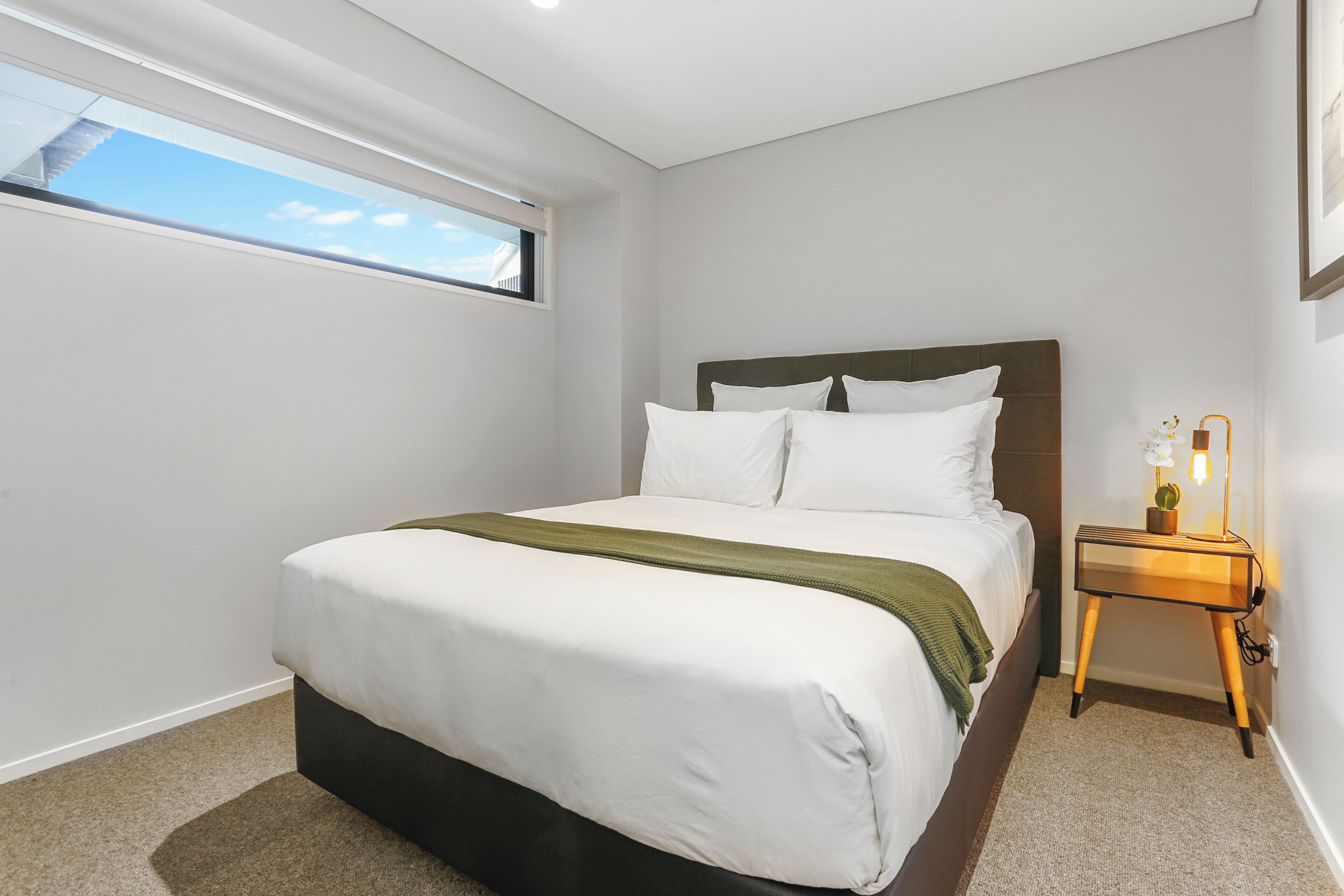 Un dormitorio con cama, mesita de noche, ventana y lámpara de pared.