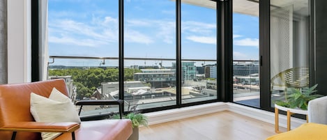 A modern living room with large windows, a leather sofa, a grey armchair, and a small table with a plant.