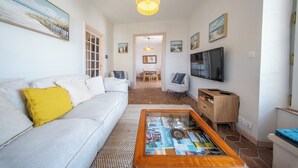 Una sala de estar con sofá, mesa de centro, televisor y obras de arte en las paredes.