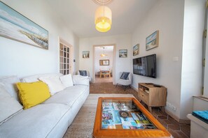 Una sala de estar con sofá, mesa de centro, televisor y obras de arte en las paredes.