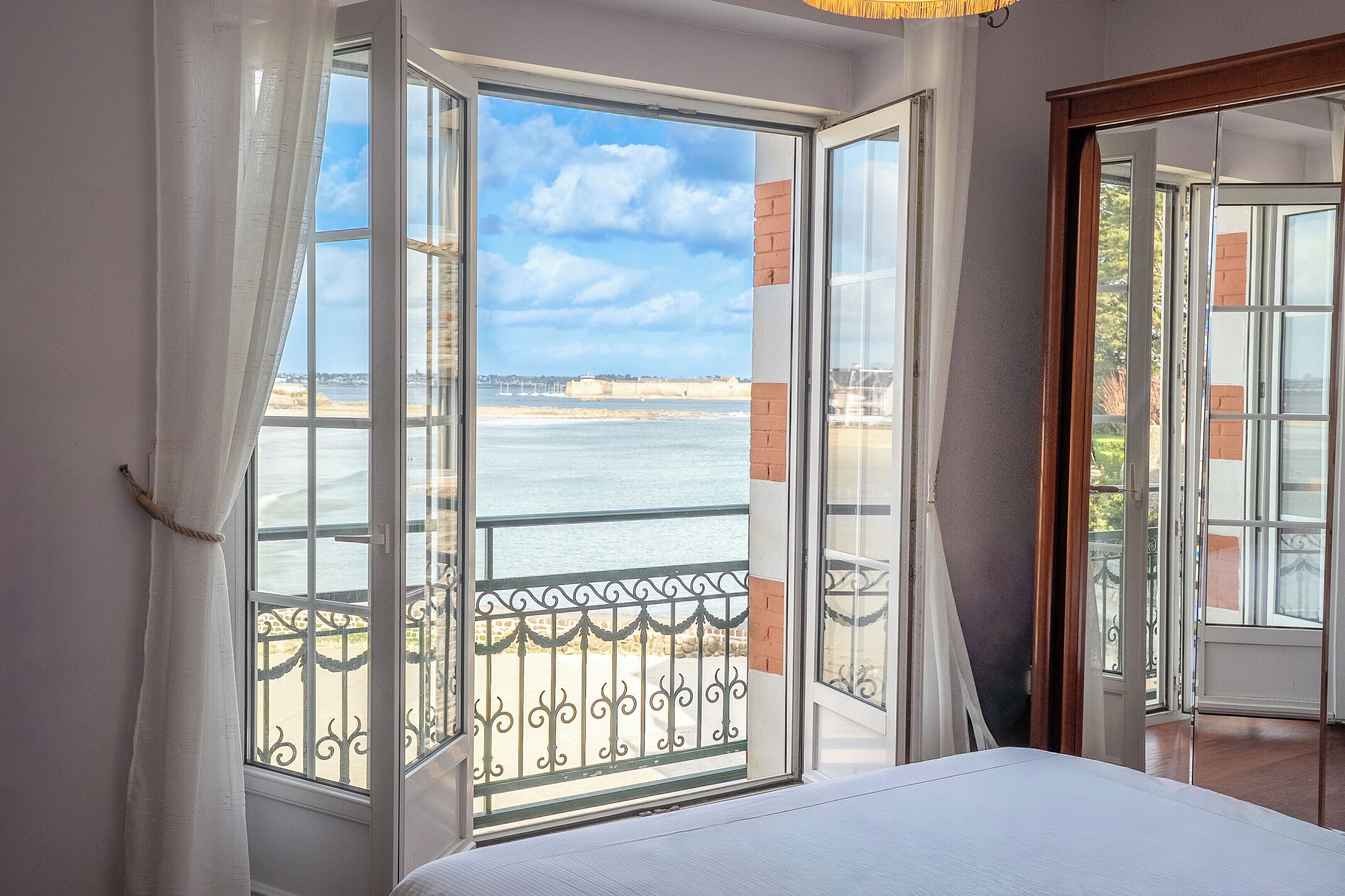 A room with a large window, a bed, and a view of the sea.