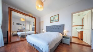 Un dormitorio con una cama grande, un espejo, una mesita de noche y una puerta que da a otra habitación.