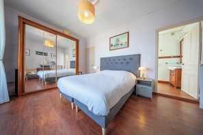 Un dormitorio con una cama grande, un espejo, una mesita de noche y una puerta que da a otra habitación.